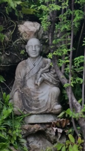 A charming monk figure sits nestled in some greenery